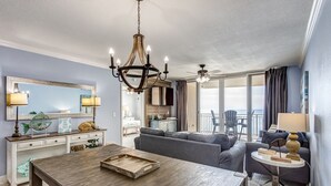 Una sala de estar moderna con una mesa de comedor de madera, una araña y vista al océano a través de grandes puertas corredizas de vidrio.