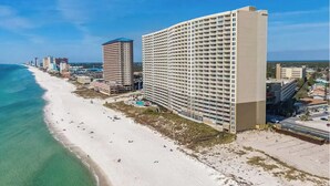 Un hotel frente a la playa con varios edificios altos, una playa arenosa y un cielo azul despejado.