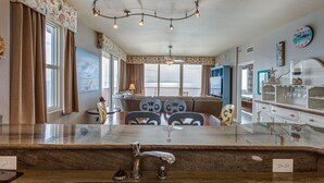 A spacious living area with a large window overlooking the ocean, a dining table with chairs, a kitchen area with a sink, and a ceiling light fixture. - 3 Bedroom in Shores of Panama - Penthouse with amazing views! (Panama City)