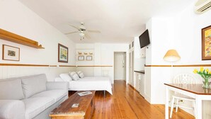Una habitación moderna y bien iluminada con un sofá gris, una mesa de centro de madera, un escritorio blanco con una lámpara y un ventilador de techo.