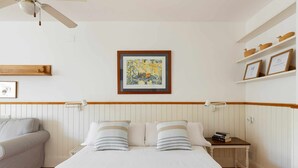Un dormitorio con cama, mesitas de noche, ventilador de techo y estante en la pared con objetos decorativos.