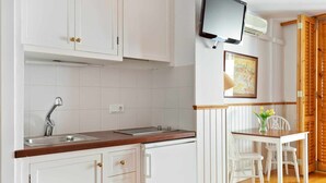 Una cocina con armarios blancos, encimera de madera, estufa empotrada, un lavamanos y un televisor sobre la estufa.