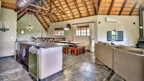 A spacious living area with a high ceiling, a dining table, a sofa, and a kitchen area with a refrigerator and sink.