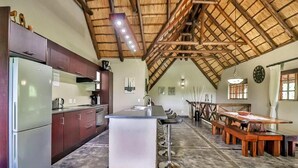 A spacious kitchen with a central island, wooden dining table, and a high ceiling with exposed beams.