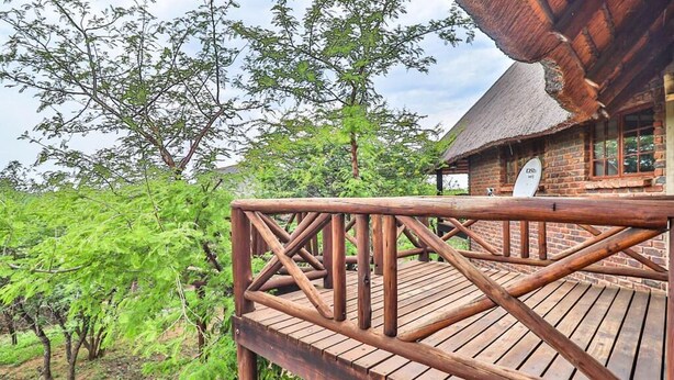 A wooden deck with a thatched roof structure, surrounded by lush greenery and trees.