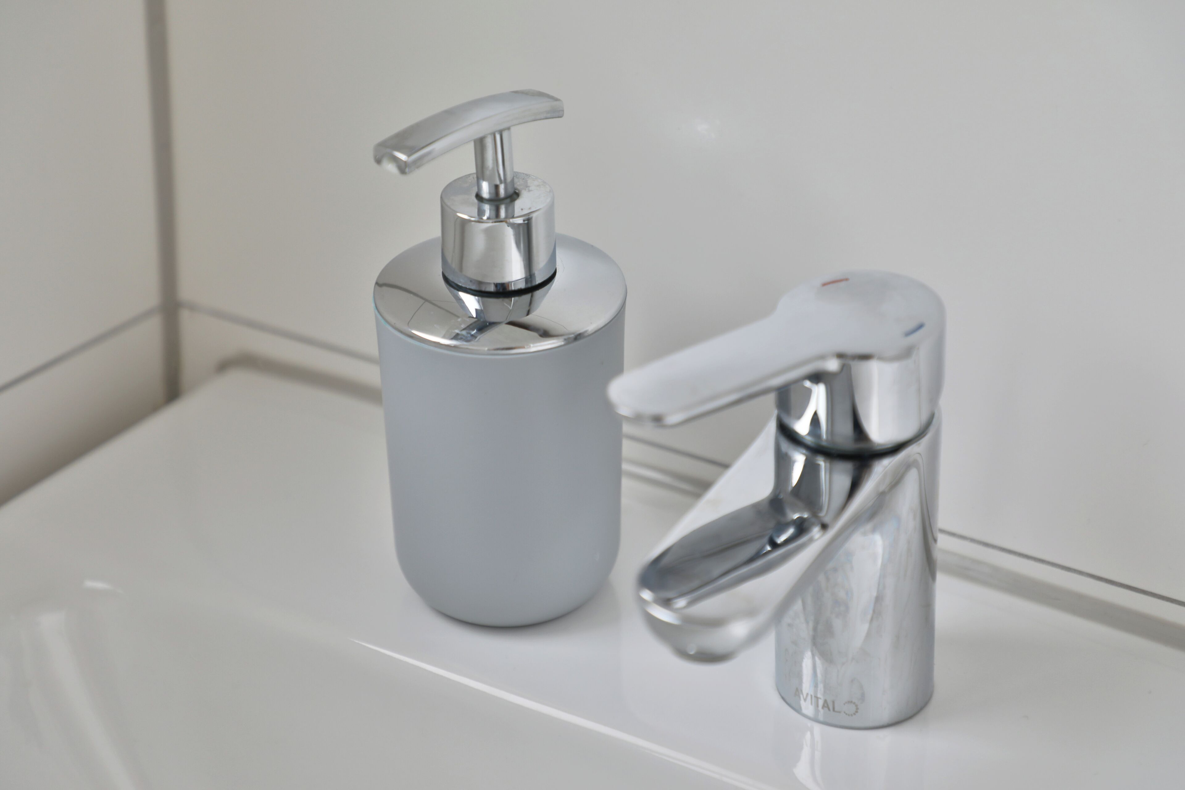 A bathroom with a white sink, a silver soap dispenser, and a chrome faucet.