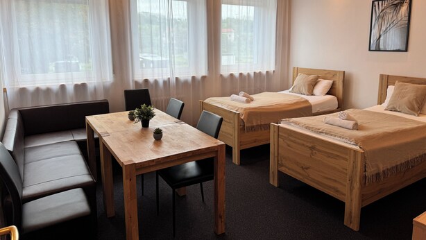 Une chambre d’hôtel avec deux lits en bois, une table en bois avec des chaises, un canapé et une plante en pot.