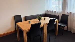 Un coin repas avec une table en bois et des chaises noires, une petite plante en pot et une fenêtre ornée de rideaux légers.