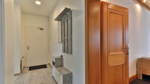 Un couloir avec une porte en bois, une porte blanche et un banc.