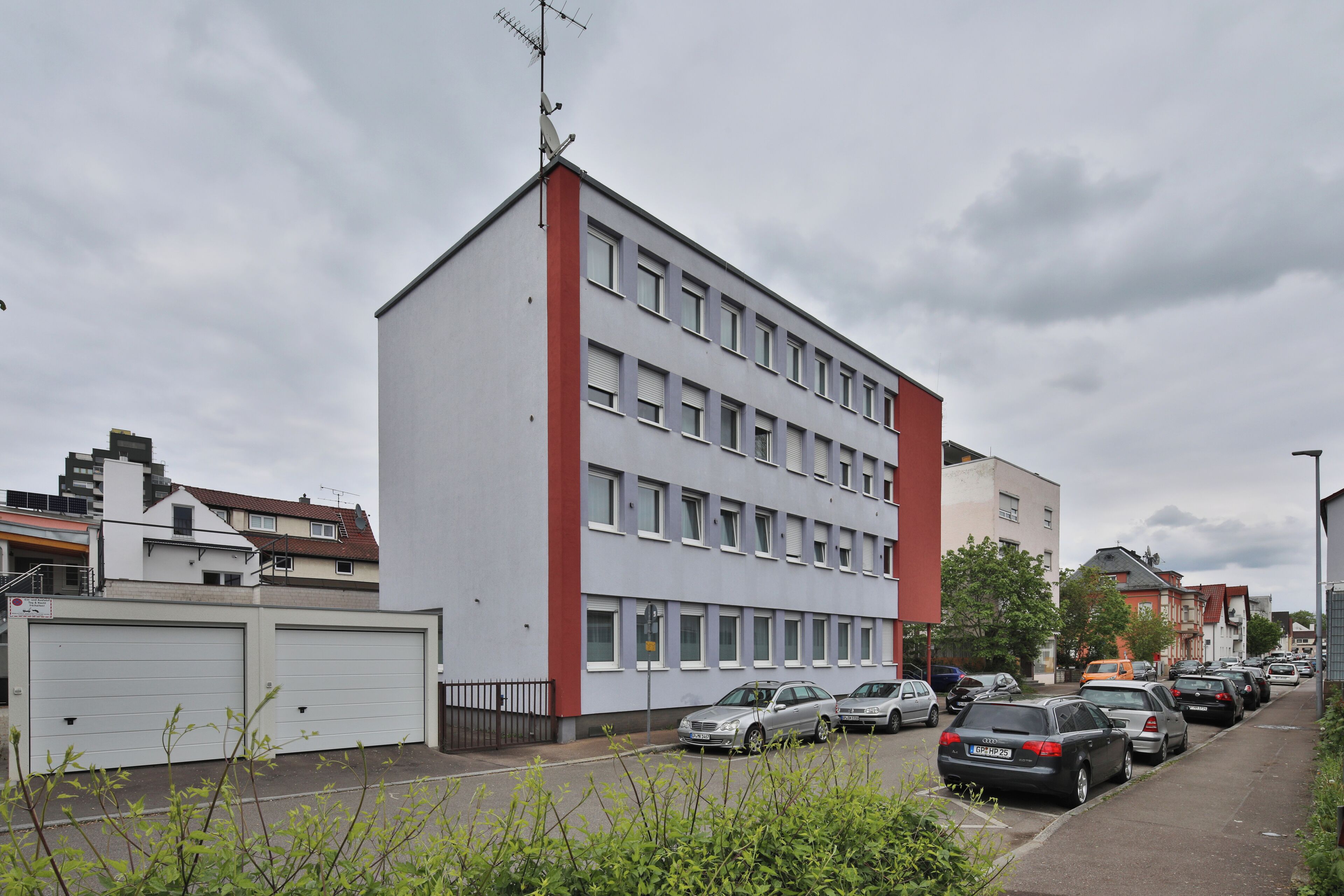 A multi-story building with a flat roof, large windows, and a red accent on the corner.