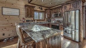 Eine Küche mit Holzschränken, einer Marmorarbeitsplatte, Edelstahlgeräten und einer integrierten Kochinsel mit Barhocker.