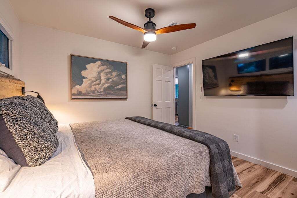 Een slaapkamer met een bed, een plafondventilator, een schilderij en een aan de muur bevestigde televisie.