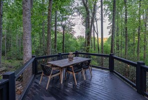 Eine Holzterrasse mit Tisch und Stühlen, umgeben von hohen Bäumen.