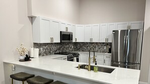 A modern kitchen with white cabinets, stainless steel appliances, a marble backsplash, and a bar area with stools.