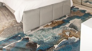 A bedroom with a bed, a ceiling fan, a large mirror, and a patterned rug.