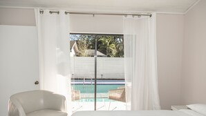 A bedroom with a bed, a chair, and a view of a swimming pool through a glass door.