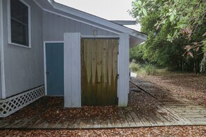 A wooden shed with a blue door, surrounded by a wooden deck and leaf-covered ground. - Atlantic Shanty - Quaint 3 BR Oceanside home in Southern Shores (Southern Shores)