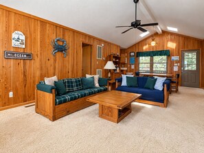 A cabin interior with two sofas, a coffee table, a ceiling fan, and a sign indicating the direction to the ocean. - Hameljuice - Classic 3 BR Oceanside Beach Cottage - close to beach (Southern Shores)