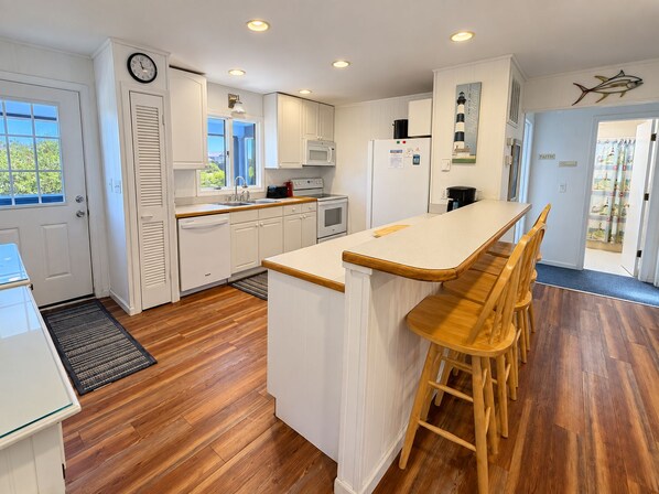 A kitchen with white cabinetry, a wooden island with bar stools, a clock on the wall, and a view of the outdoors through the window.