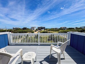 A deck with white chairs and a table, overlooking a coastal area with houses and a clear sky.