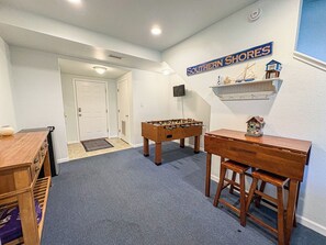 A room with a foosball table, a wooden desk, and a shelf with a model ship.