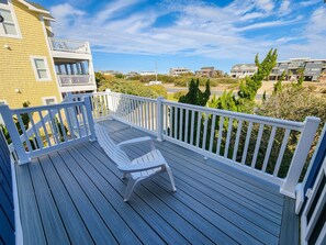 Une terrasse en bois avec une chaise en plastique blanche, des rampes blanches et une vue sur des immeubles d’habitation en arrière-plan.