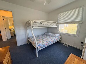 Quarto com beliche, janela, piso coberto por carpete e porta que dá para outro quarto.