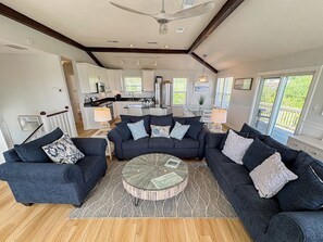 Ein modernes Wohnzimmer mit Ecksofa, rundem Couchtisch und Blick auf die Küche sowie den Außenbereich.