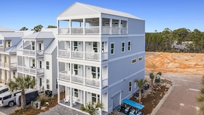 A multi-story building with balconies, a covered parking area, and a construction site in the background. - Dusk Til Dune - Vacation Home Near the Beach with Shared Pool (Santa Rosa Beach)