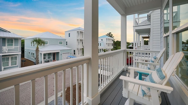 A coastal residential area with white houses, a wooden deck, and a view of the ocean. - Dusk Til Dune - Vacation Home Near the Beach with Shared Pool (Santa Rosa Beach)