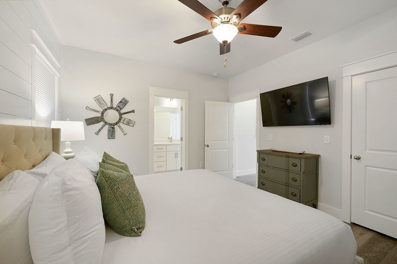 Une chambre à coucher comprenant un lit, un ventilateur de plafond, un téléviseur, une commode et une horloge murale.