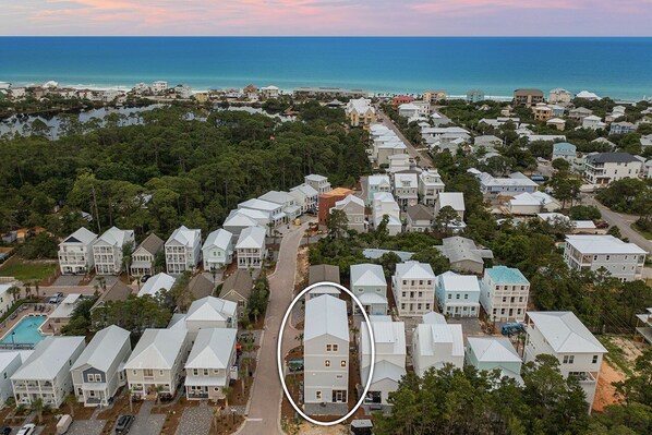 An aerial view of a coastal residential area with multiple houses, a swimming pool, and a clear view of the ocean.