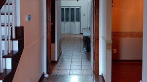 Un pasillo con una escalera a la izquierda, un ventilador de techo y una vista a una habitación con un armario y un cubo de basura.