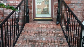 Una escalera de ladrillo que lleva a una puerta con un panel de vidrio, flanqueada por barandillas de hierro negro.