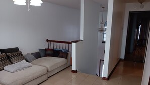Un salón con un sofá color crema, cojines estampados, una escalera de madera y un candelabro.