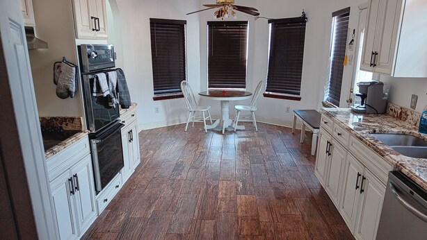 Una cocina con armarios blancos, una mesa de comedor con sillas y un ventilador de techo.