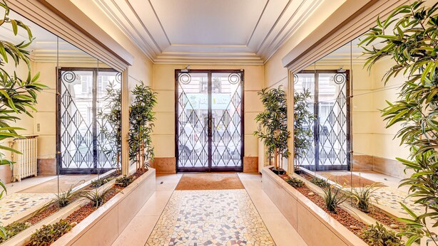 A corridor with a tiled floor, mirrored walls, and potted plants.