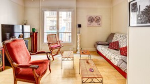 A living room with a red armchair, a wooden chair, a sofa with patterned cushions, a small table with glasses, and a globe map on the wall.