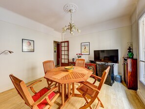 Uma área de refeições com mesa e cadeiras de madeira, um lustre, uma televisão e obras de arte nas paredes.