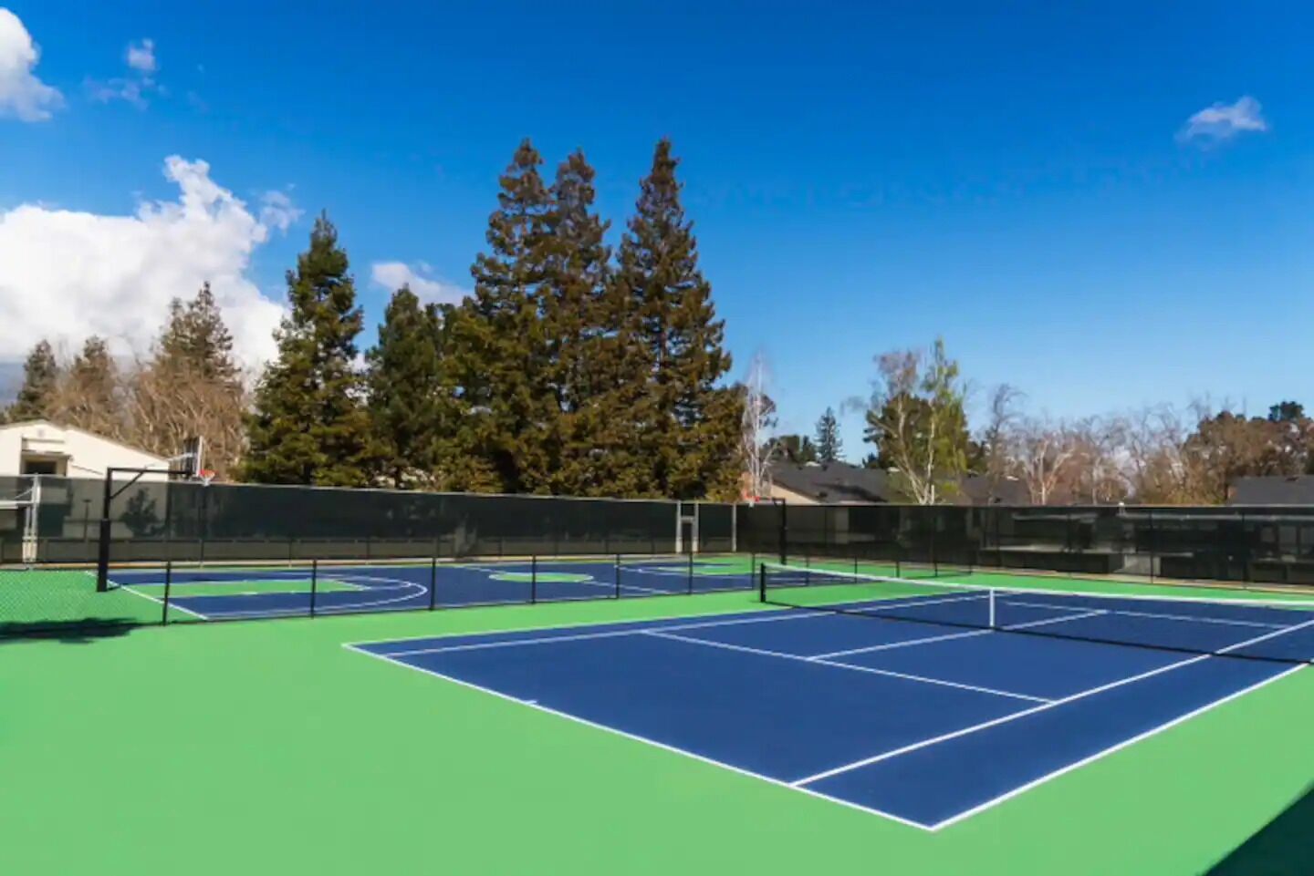 An outdoor tennis court with a net, surrounded by trees and houses.