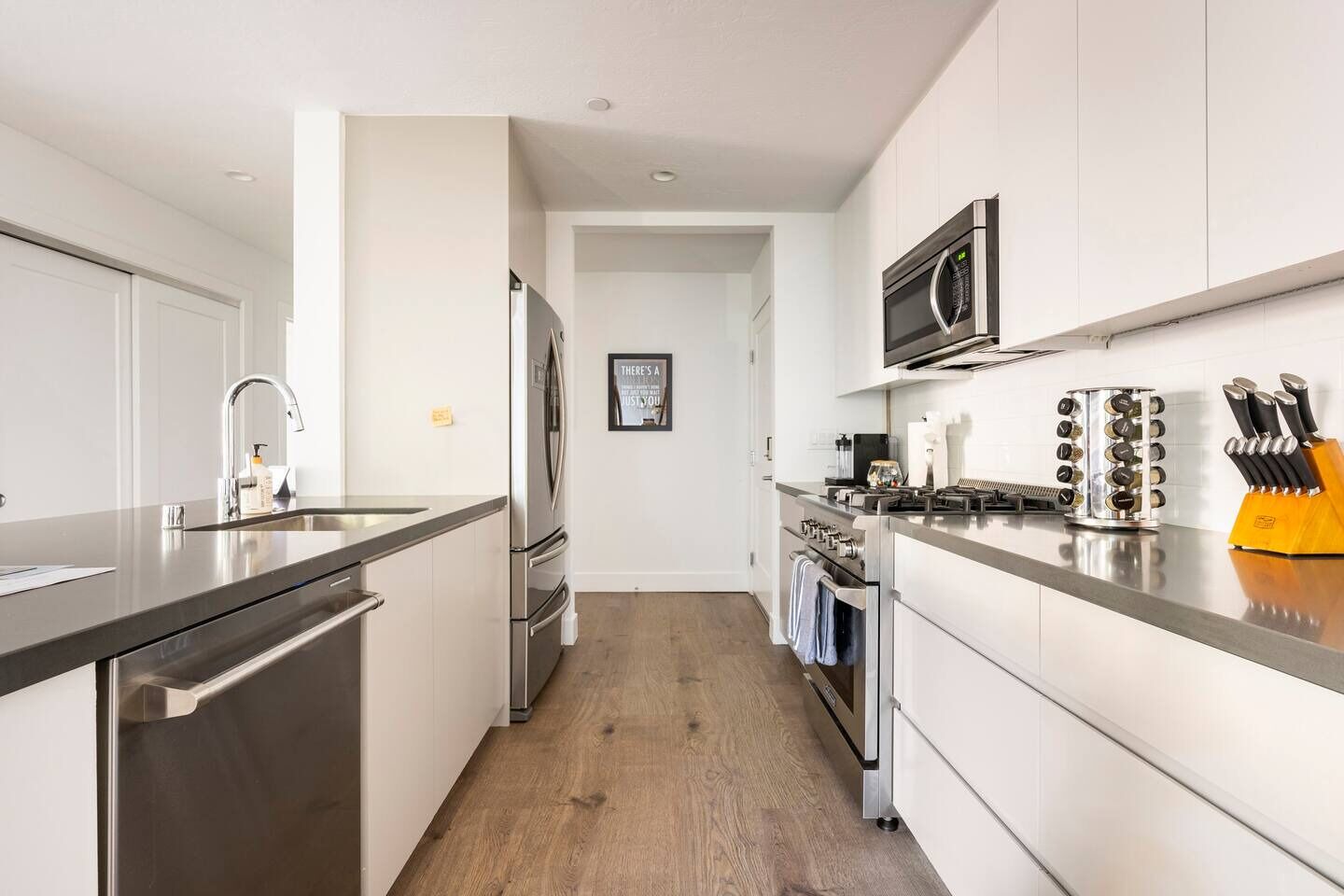Una cocina moderna con electrodomésticos de acero inoxidable, piso de madera y un bloque para cuchillos amarillo.