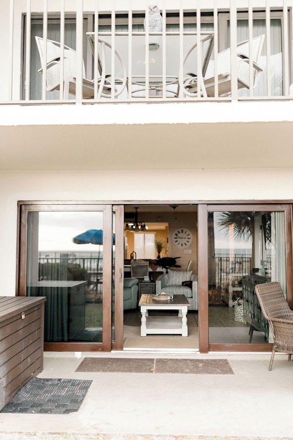 A modern apartment with a balcony, furnished with white chairs and a wicker chair, and a dining area with a table and chairs.