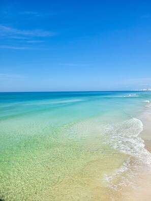 A beach with clear shallow waters and a distant city skyline.