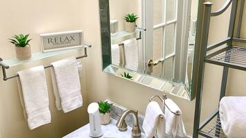 A bathroom with a marble sink, a large mirror, a towel rack with two towels, a shelf with a plant, and a sign that says "RELAX".