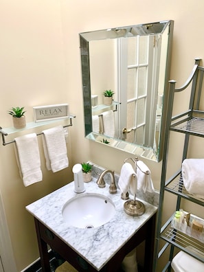 A bathroom with a marble sink, a large mirror, a towel rack with two towels, a shelf with a plant, and a sign that says "RELAX". - Suites On King (Niagara-on-the-Lake)