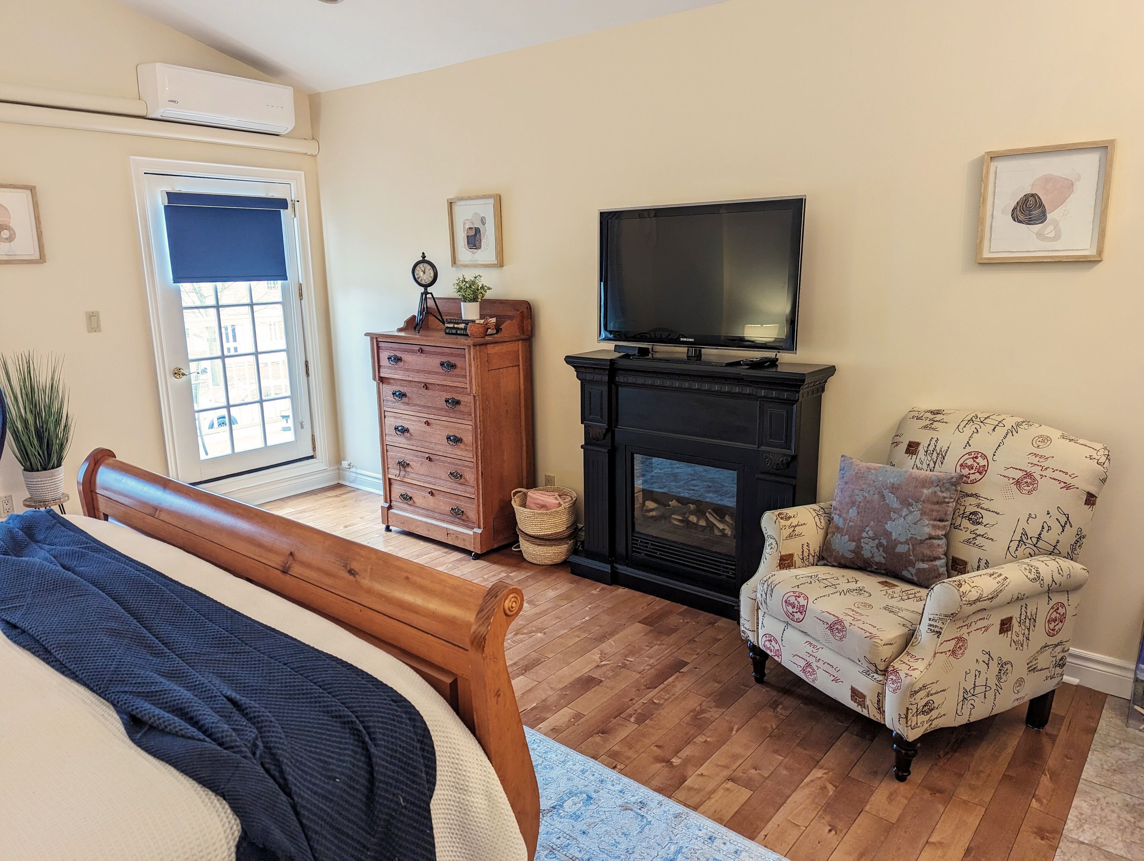A cozy living room with a fireplace, a television, a bed, and a chair with a signature pattern upholstery.