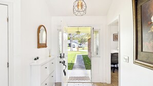 Un couloir avec une porte blanche, une armoire blanche, un miroir et un carillon.
