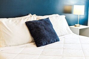 Comfortable bed with a white quilted cover and two pillows, set against a serene backdrop.