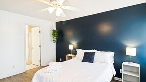 Une chambre à coucher avec un lit, deux tables de chevet, un ventilateur de plafond et un mur d’accent bleu foncé.