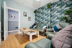 Relax in this stylish living room with a green leather sofa, patterned wallpaper, and a wooden coffee table.
